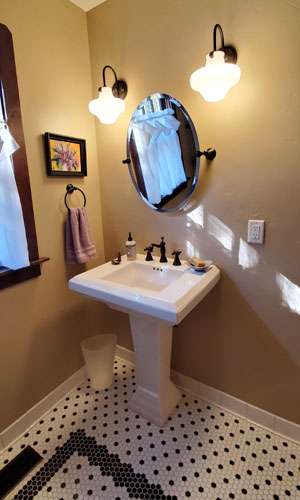 Photo of pedestal sink, historic sconces and black and white penny tile floor