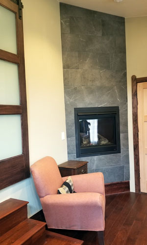 photo of corner fireplace with floor to ceiling grey stone tile and a warm wood floor