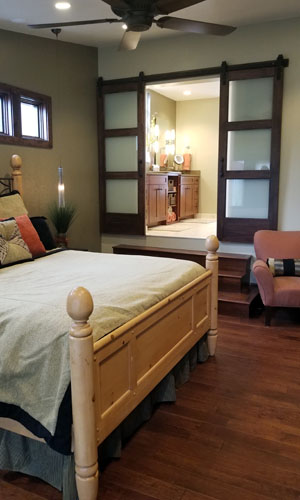 photo of bedroom with ceiling fan looking into bathroom that has double sliding barn doors with frosted glass