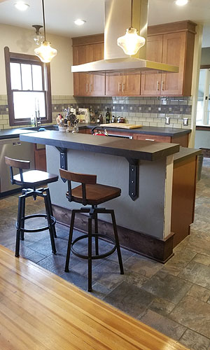 photo of kitchen island with raised countertop, bar stools, a stainless steel hood vent, slate and wood floors