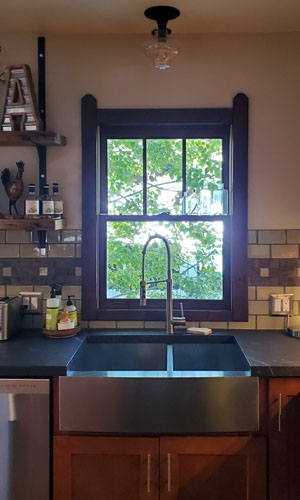 photo of kitchen window behind stainless steel farmhouse sink with chrome gooseneck faucet and historic pendant above