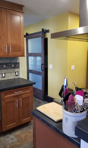 Photo showing sliding barn door with frosted glass beyond kitchen with warm wood cabinets