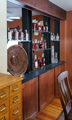 Photo of see-through wall with wood cabinets below, wood beam above, and metal columns and shelves between with bottles on them