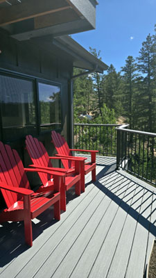 photo of exterior deck with bright red adirondack chairs and metal and wood railings with fir trees