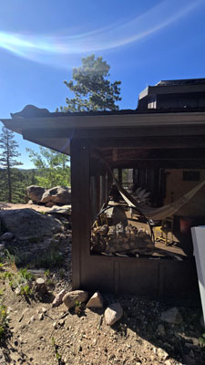 photo of exterior of screened porch with wood log storage and trees and rocks beyond