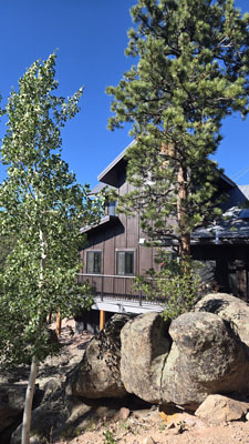 photo of exterior of brown board and batten two story house with large rocks and fir trees