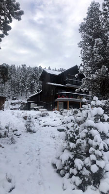 photo of tall brown house with balconies surrounded by trees all covered in snow