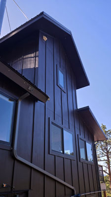 photo looking up at house with brown board and batten siding and varying sloped roofs
