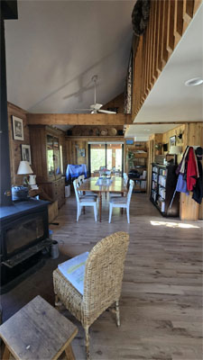 photo of dining room in rustic cabin with loft above, wood beam and freestanding fireplace stove