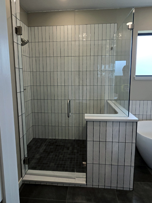 photo of a shower with a bench concealed behind a half wall that's tiled with a seamless shower door and white vertical tile