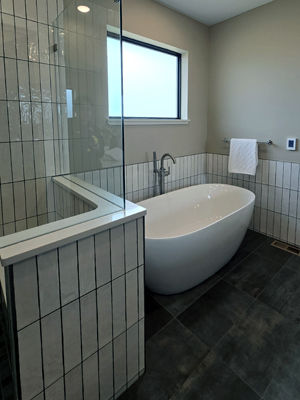 photo of bathroom with freestanding tub, frosted window, and a partial shower wall with vertical white tile