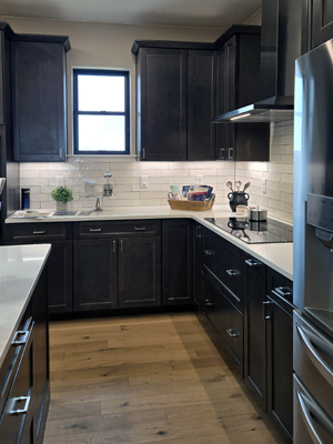 photo of kitchen with window, dark cabinets, a cooktop, and white tile backsplash