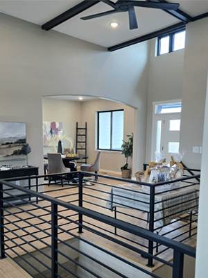 photo of house with vaulted ceiling with dark wood beams, ceiling fan, and black metal railings around a stair opening