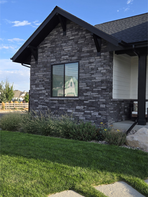 photo of part of house with gable roof with wood brackets, dark trim and grey stacked stone