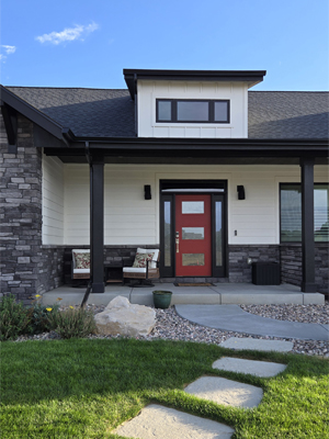 photo of front porch with red door with transom and sidelites, dormer window above and grey stone