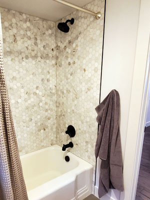 photo of tub shower with black fixtures, stone honeycomb tile