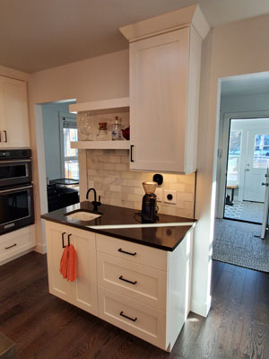photo of kitchen beverage station with stone subway tile backsplash, black quartz countertops and bar sink