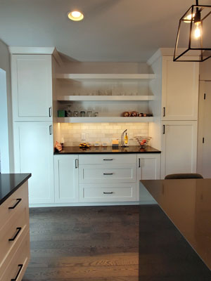 photo of kitchen storage area with white cabinets and shelves and black countertops