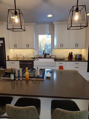 photo of kitchen over cooktop island to farmhouse sink with window, stone subway tile backsplash