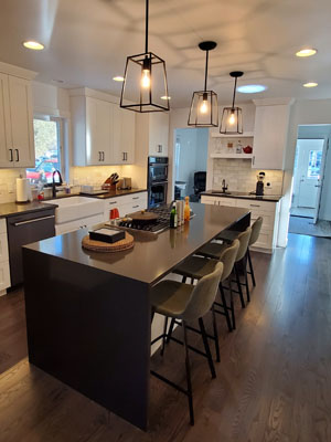 photo of kitchen island with cooktop, black stainless dishwasher, black waterfall countertops