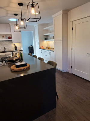 photo of kitchen with black frame pendants, black waterfall countertop island, white cabinets and dark wood floors
