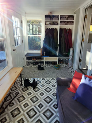 photo of sunroom mudroom with coats hanging a bench and cubbies and a blue geometric tile floor